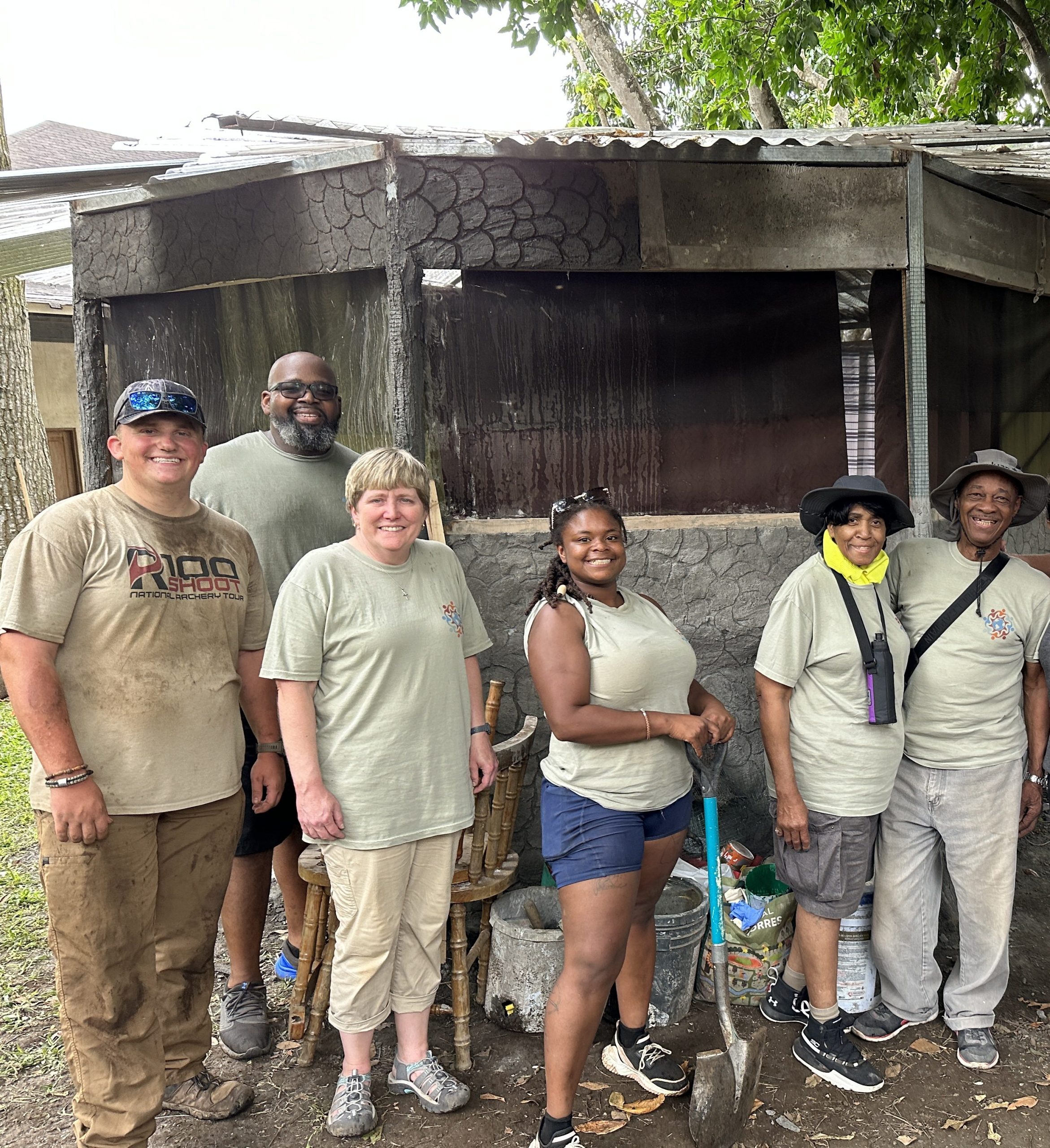 Group of volunteers stand in front of cabin they built after a long hot day.