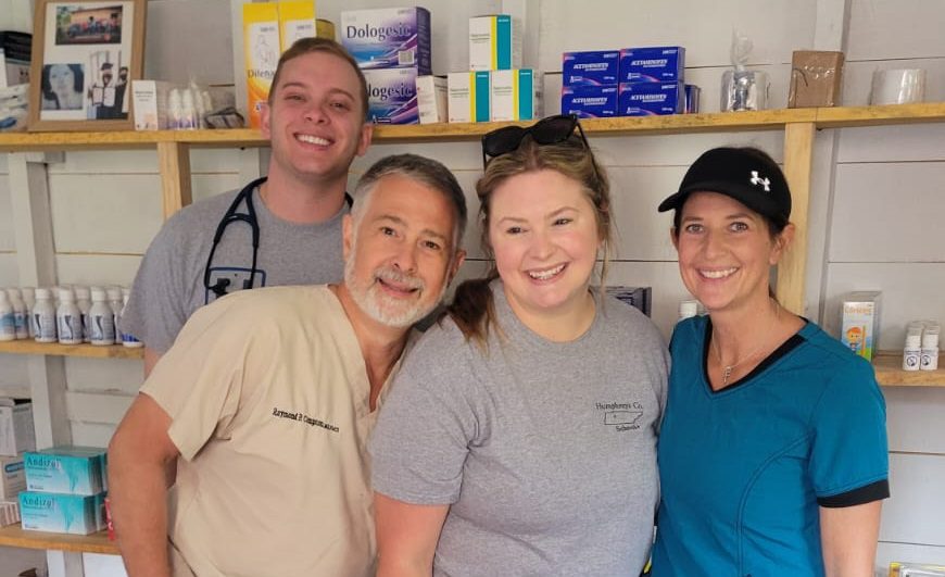 four volunteers standing in front of wall of medications