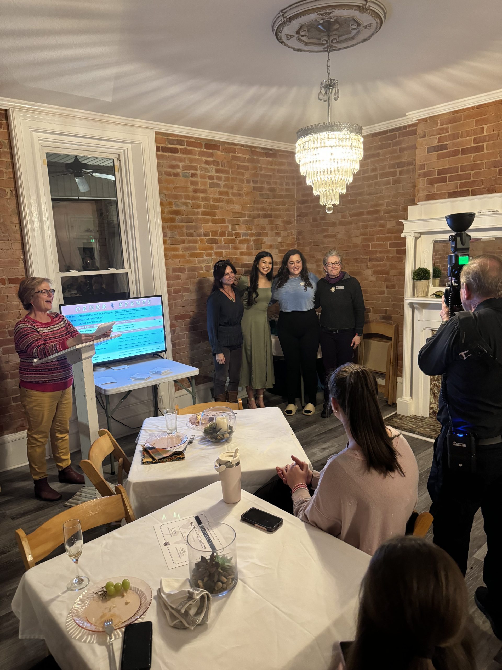 Passport Party photographer is taking a picture of one woman speaking and four women lining up for the shot