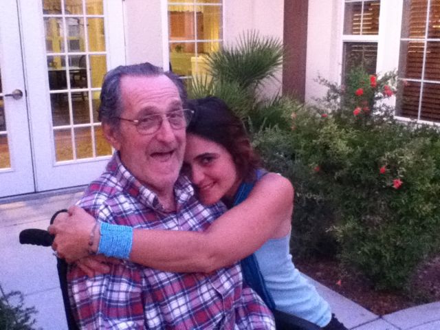 older photo of older man with young woman's arms wrapped around his neck